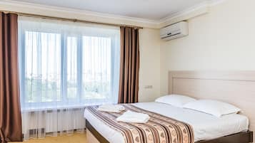 A hotel room with a bed, a window with curtains, an air conditioning unit, and a view of the outdoors.