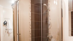 Cabina de ducha con paredes de vidrio y un diseño curvo, un lavamanos blanco y un perchero con toallas.