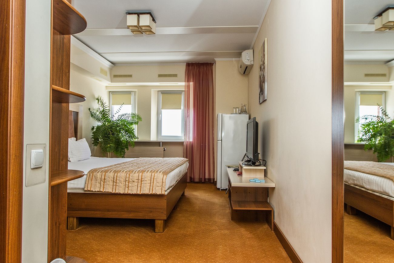 A hotel room with a wooden bed, a desk with a computer, a mirror, and a potted plant.