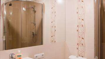 Un baño con ducha de vidrio, lavamanos con dispensador de jabón e inodoro.