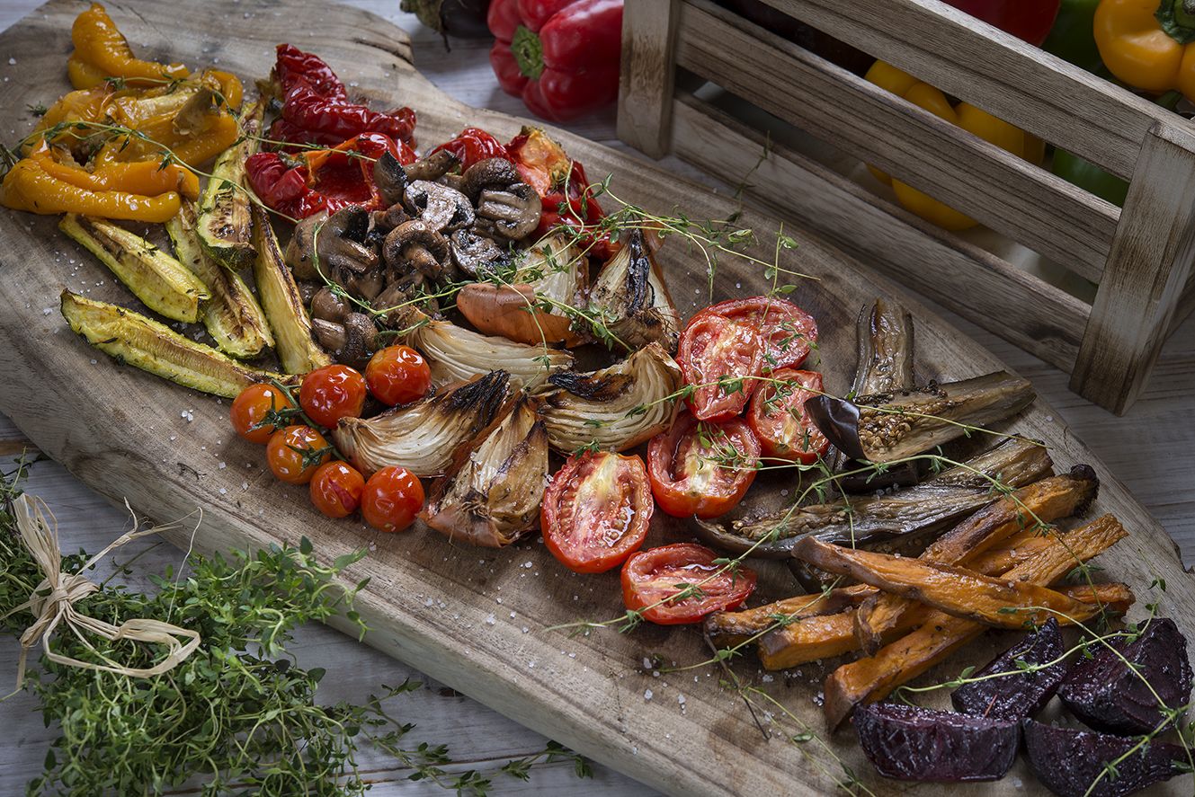 A wooden cutting board with various roasted vegetables and herbs.