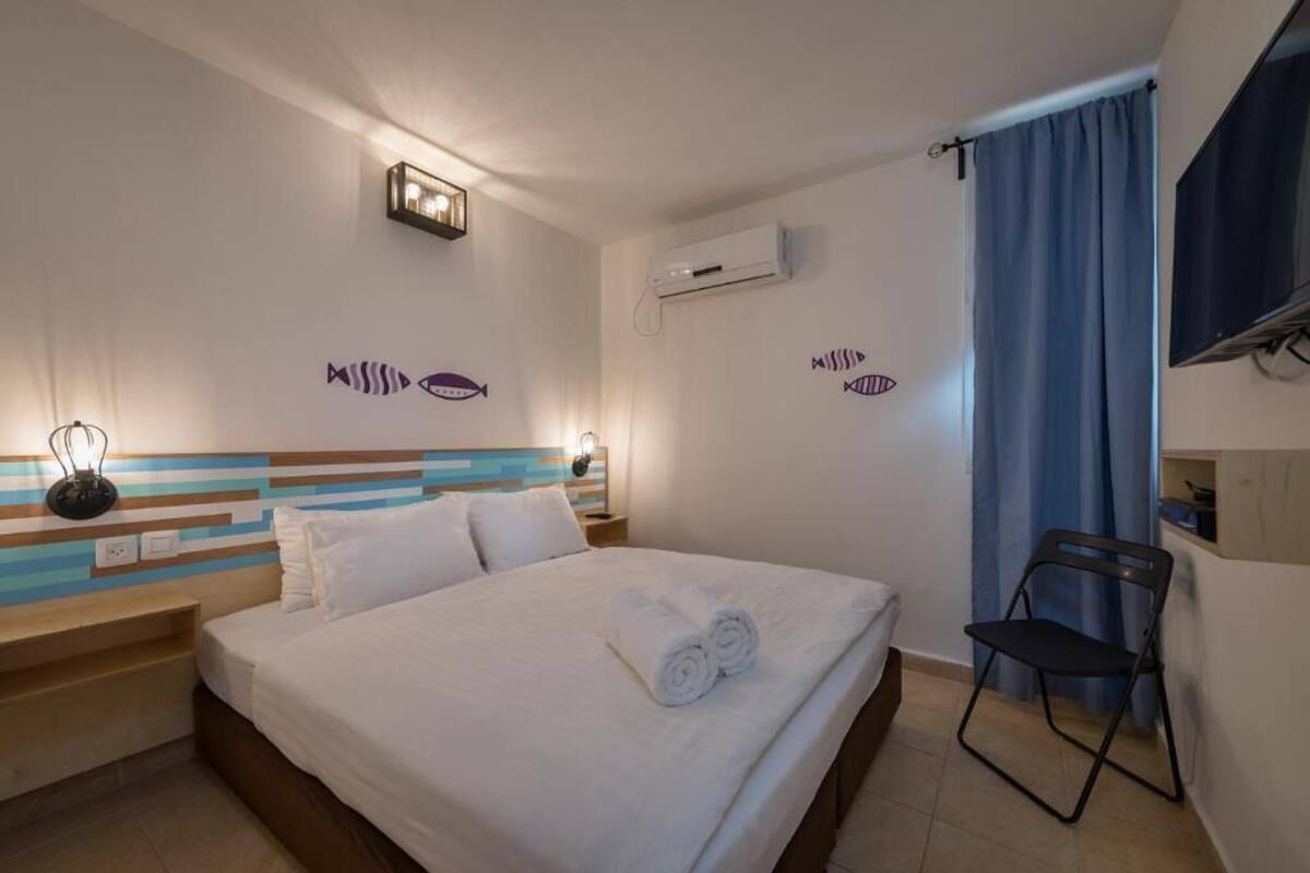 Habitación de hotel con cama, una silla, aire acondicionado mural y decoración de peces en la pared.