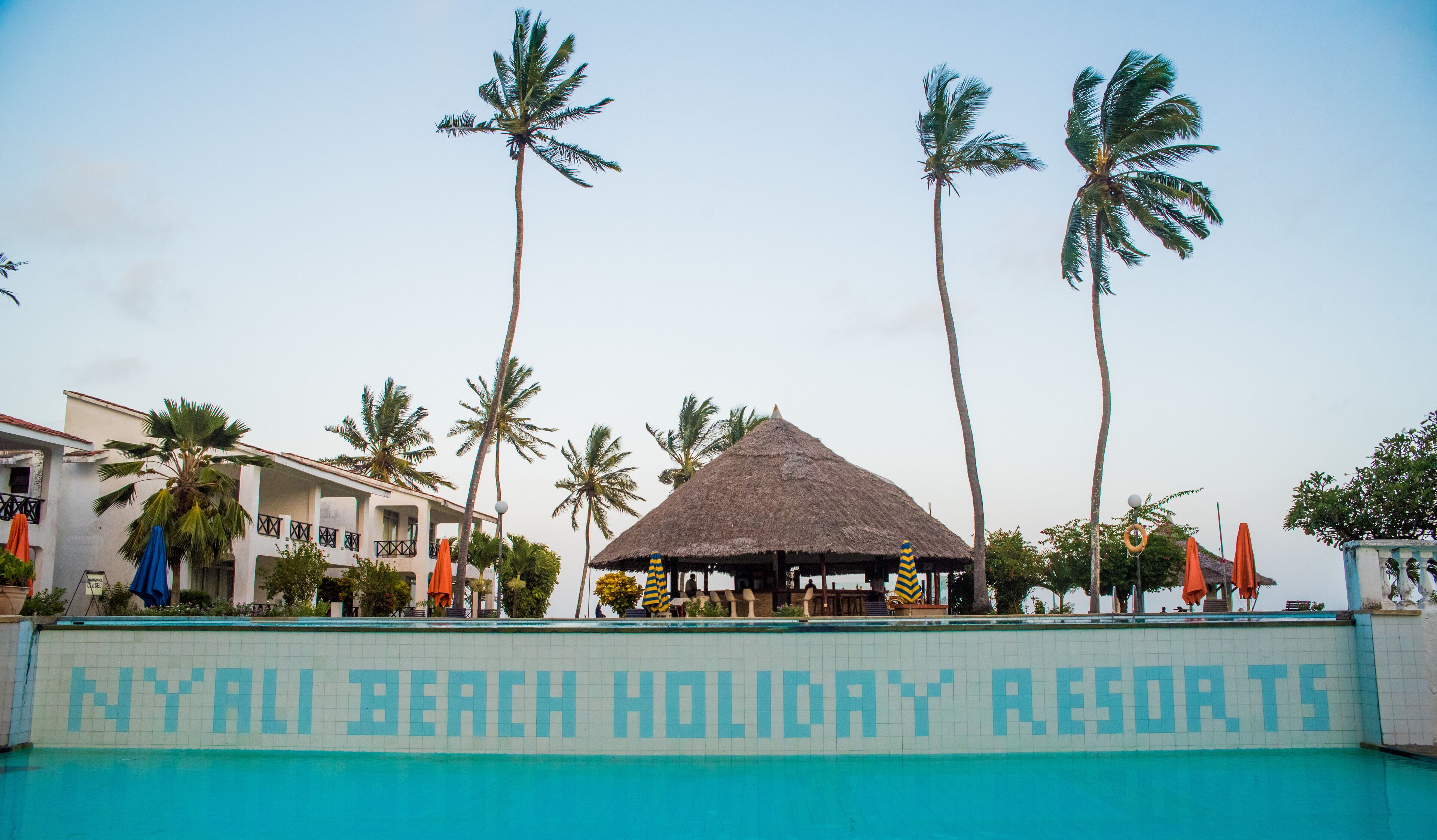 Un resort con piscina, palmeras y un edificio con techo de paja.