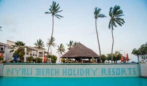 A resort with a pool, palm trees, and a building with a thatched roof.