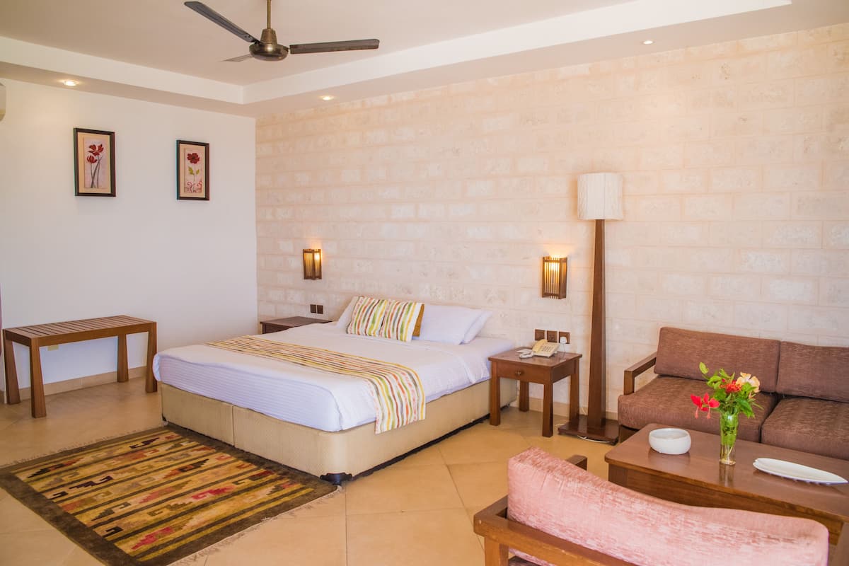 A hotel room with a bed, a sofa, a small table, a bench, and a wall-mounted lamp.