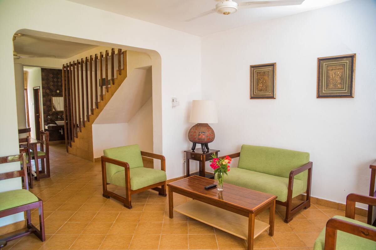 A living room with a sofa, chairs, a coffee table, a lamp, and a staircase.
