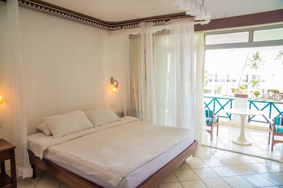 A bedroom with a bed, a nightstand, a wall-mounted light, and a view of an outdoor area with a table and chairs.