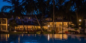 A nighttime resort with a swimming pool, palm trees, and illuminated buildings.