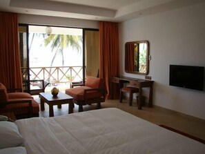 A hotel room with a bed, a desk, a chair, a TV, and a balcony with curtains.