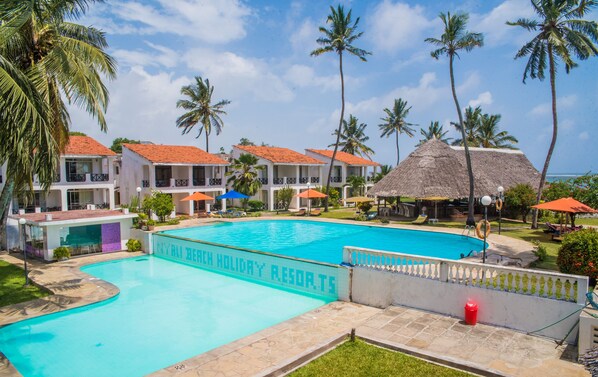 A resort with a large swimming pool, multiple buildings with balconies, and palm trees.