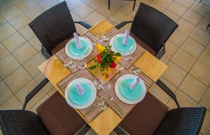 A dining table set for four with a central floral arrangement, surrounded by wicker chairs.