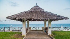 A thatched gazebo with a concrete pathway leading to it, overlooking a beach. - Nyali Beach Holiday Resort (Mombasa)