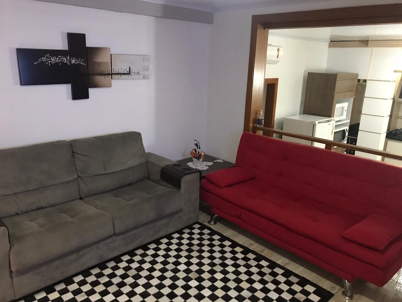 A living room with a grey sofa, a red sofa, a black and white checkered rug, and a wall-mounted artwork.