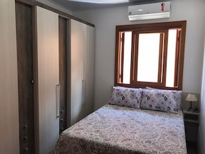 A bedroom with a bed, a wardrobe, a nightstand, and a window with curtains.