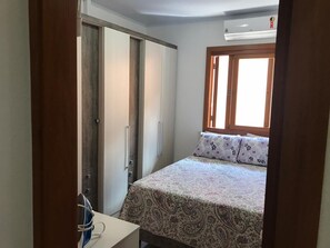 A bedroom with a bed, a wardrobe, a desk with a chair, and a window with blinds.
