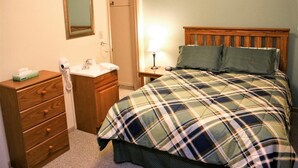 A bedroom with a wooden dresser, a bedside table with a lamp, and a bed with plaid bedding. - Cianci's Motel and Suites (Greenville)