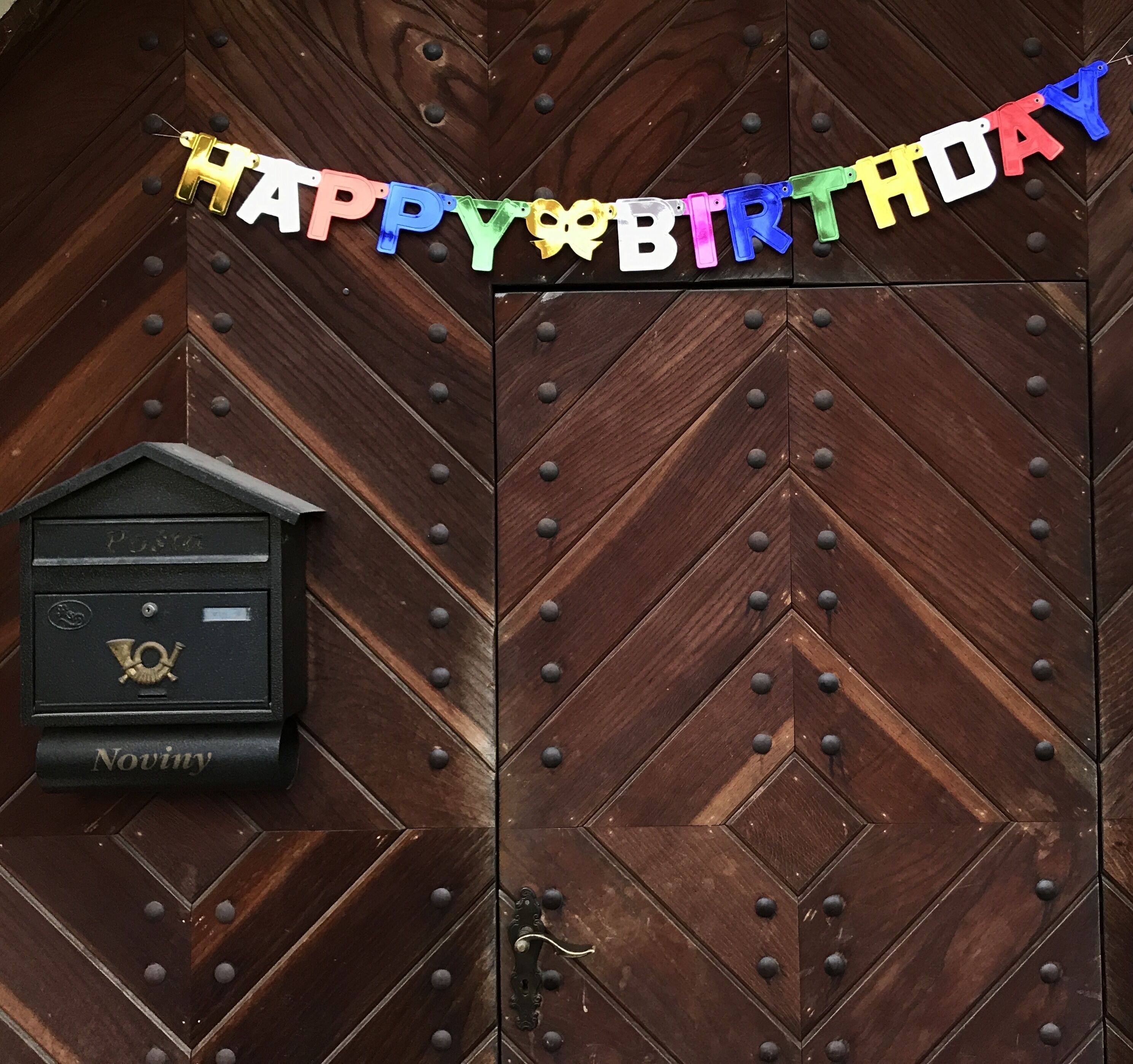 Una puerta de madera con un cartel de 'Happy Birthday' y un buzón con la palabra 'Noviny'.