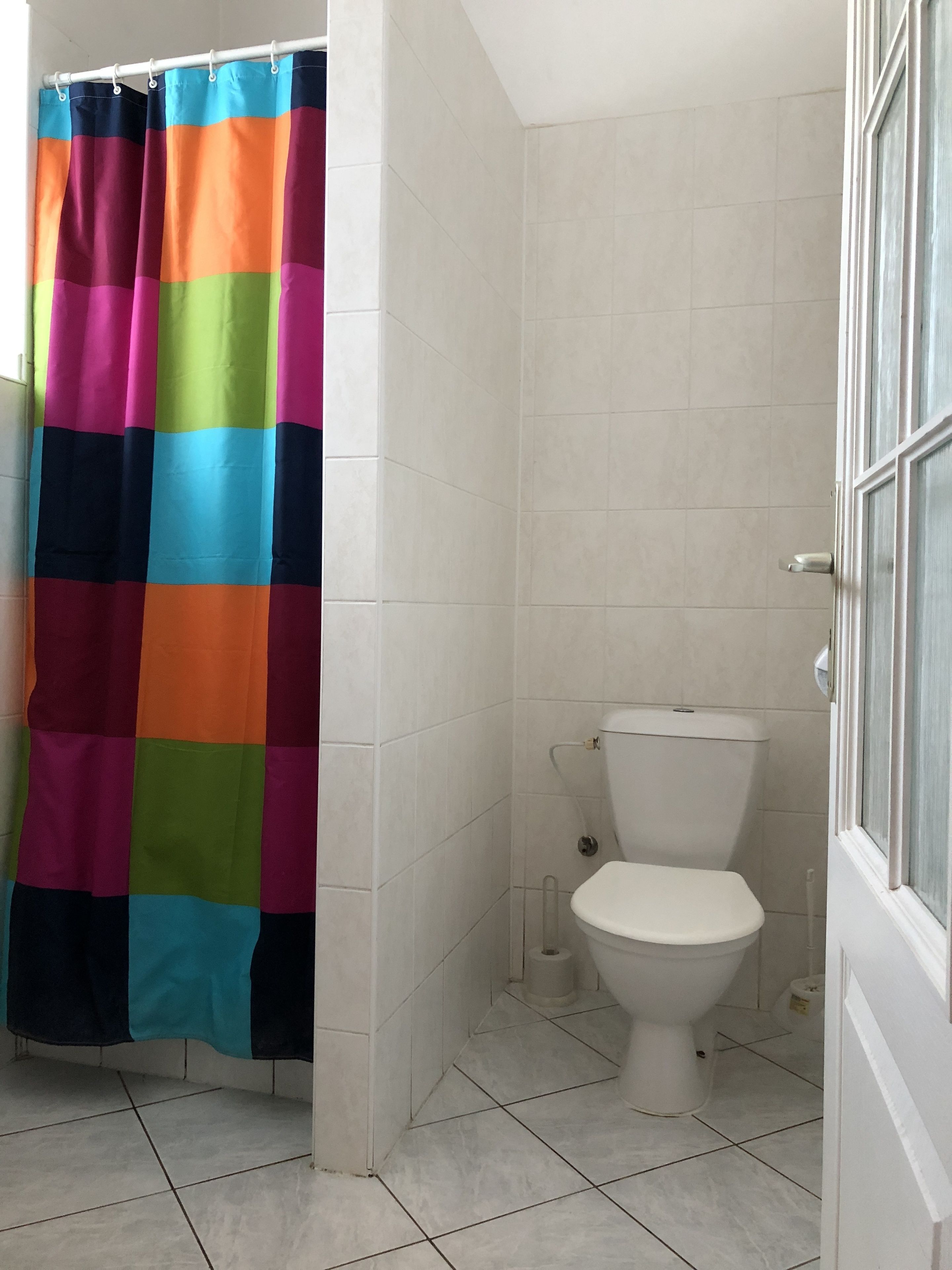 A bathroom with a white toilet, white tiled walls, and a colorful shower curtain.