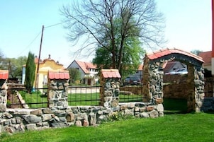 Una edificación de piedra con techo rojo, rodeada por un muro de piedra y una valla de metal.