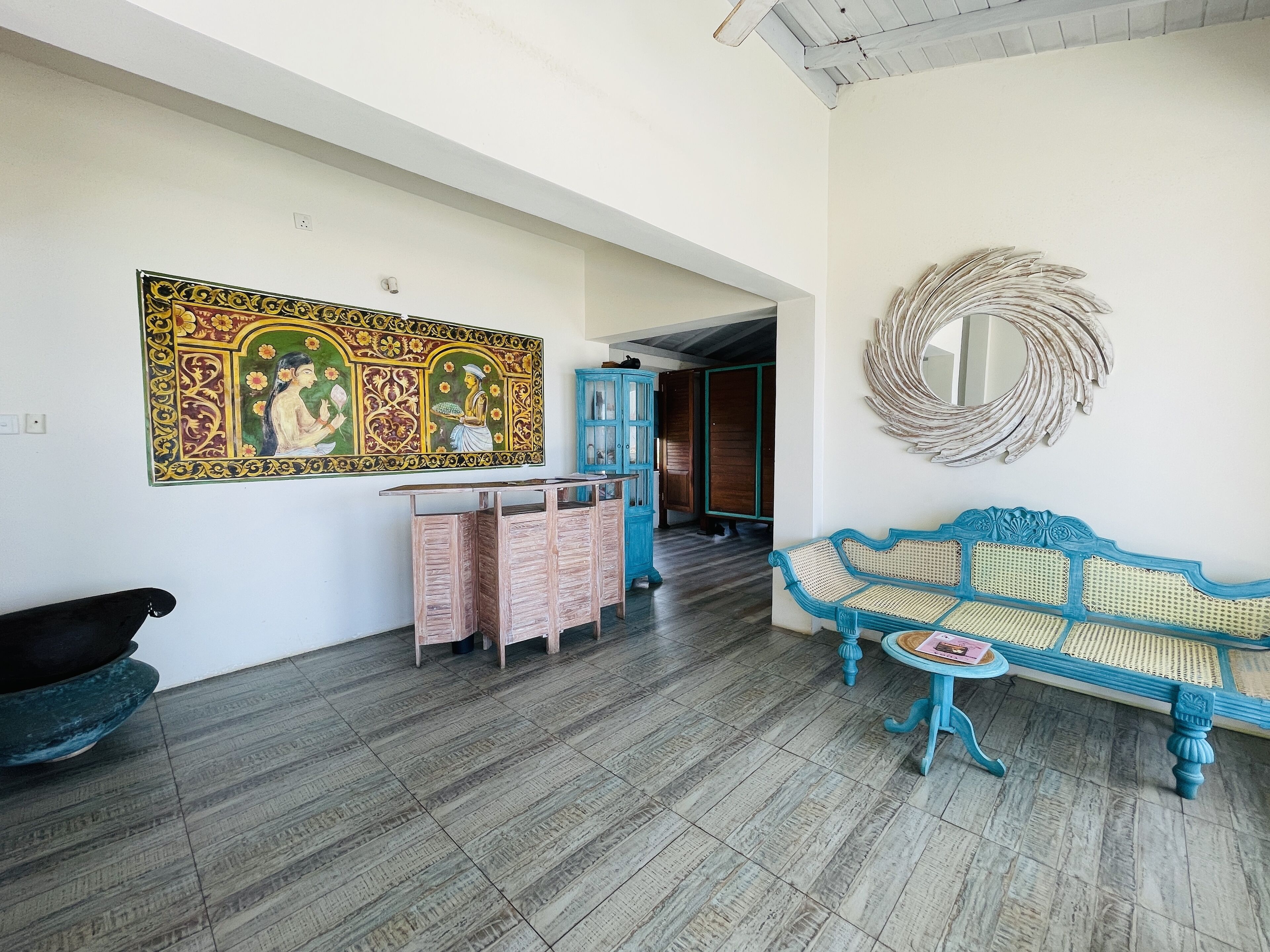 Una habitación con un cuadro decorativo grande, un sofá azul, un armario de madera y un espejo en la pared.