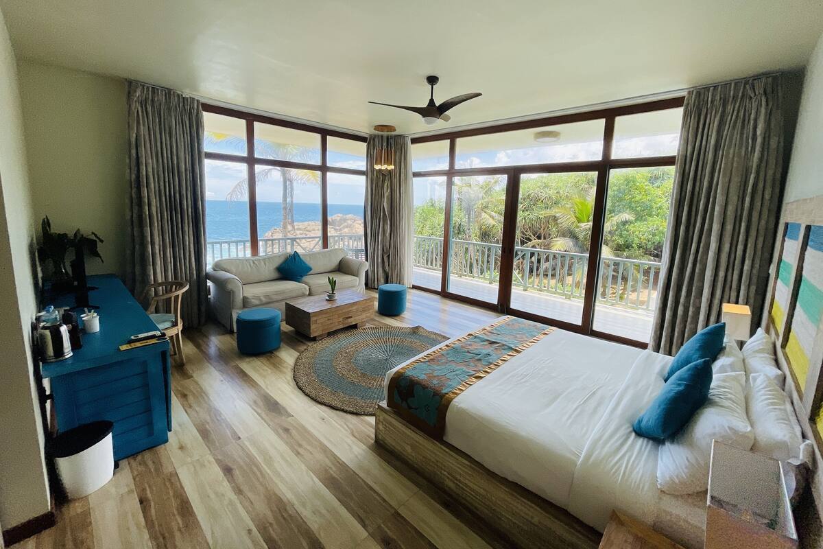 A spacious bedroom with a large bed, a sofa, a desk, and a view of the ocean.