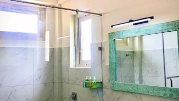 Un baño moderno con cabina de ducha de vidrio, un lavamanos blanco y un espejo con marco verde, y una lámpara en el techo.