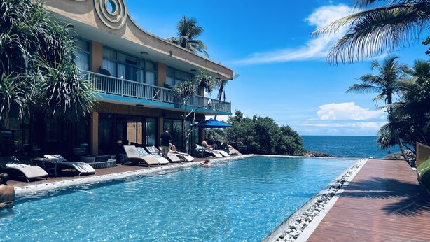 Piscina de resort con sillones reclinables y una terraza de madera, con vista al océano.