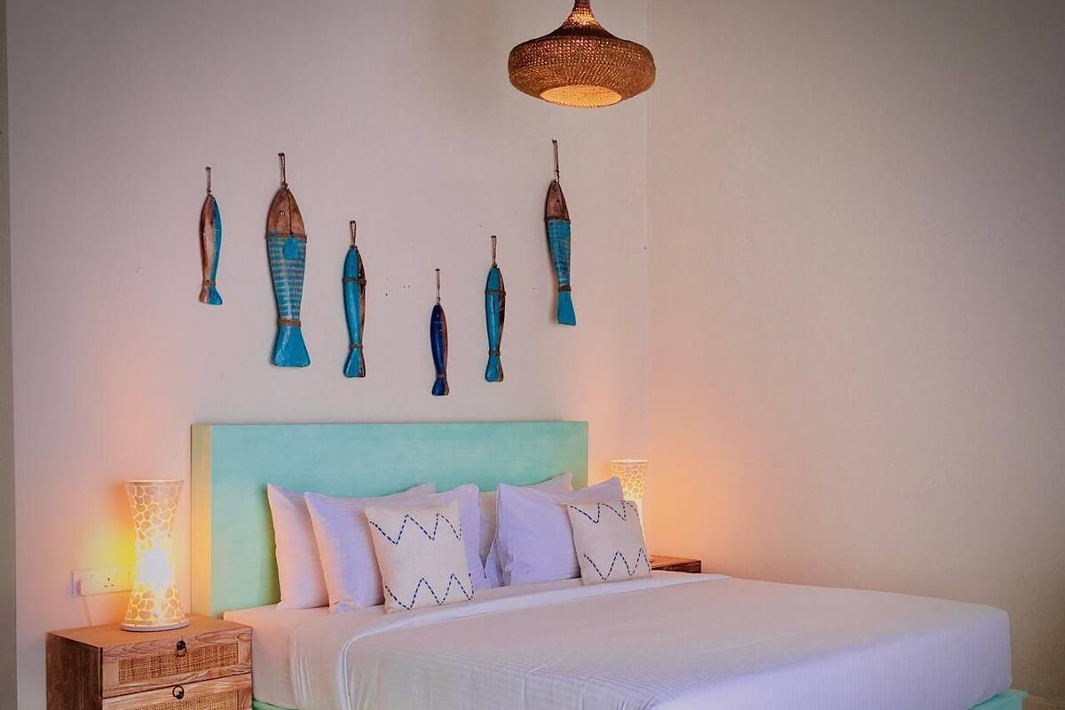 A bedroom with a teal-colored bed, white bedding, and decorative wall art.