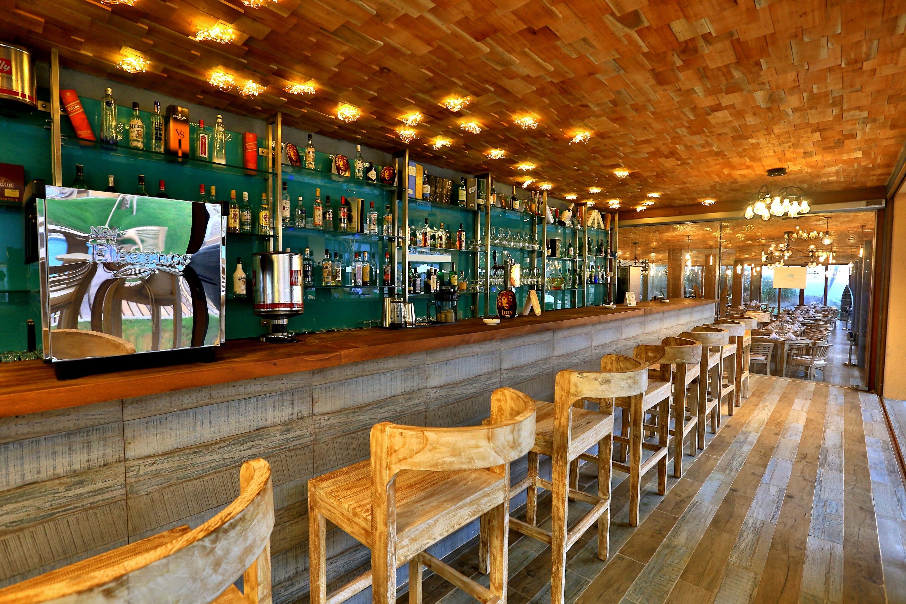 A bar area with wooden chairs, a long counter, and shelves stocked with various bottles.