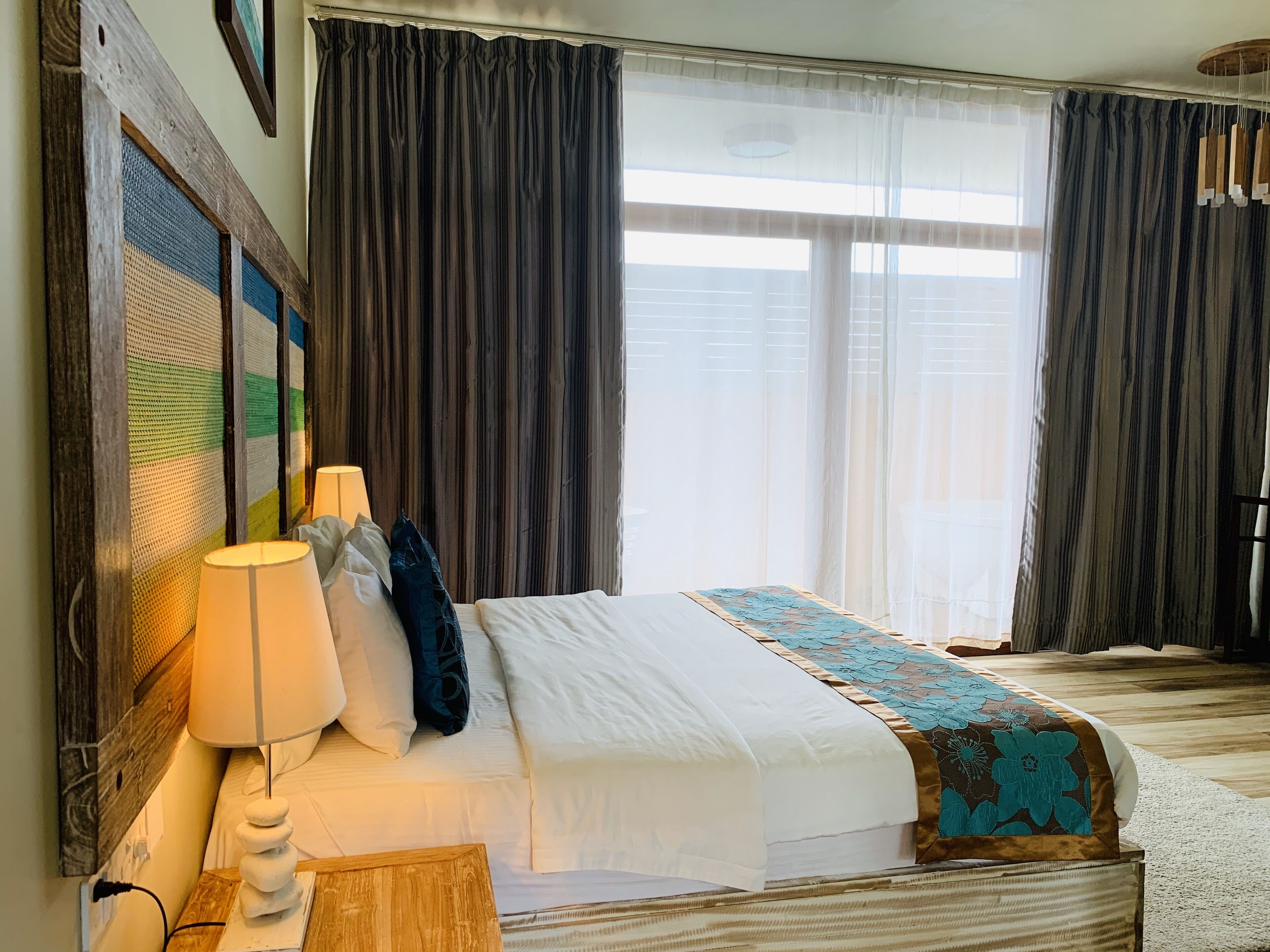 A hotel room with a large bed, a wooden headboard, a wall-mounted lamp, and a window with curtains.