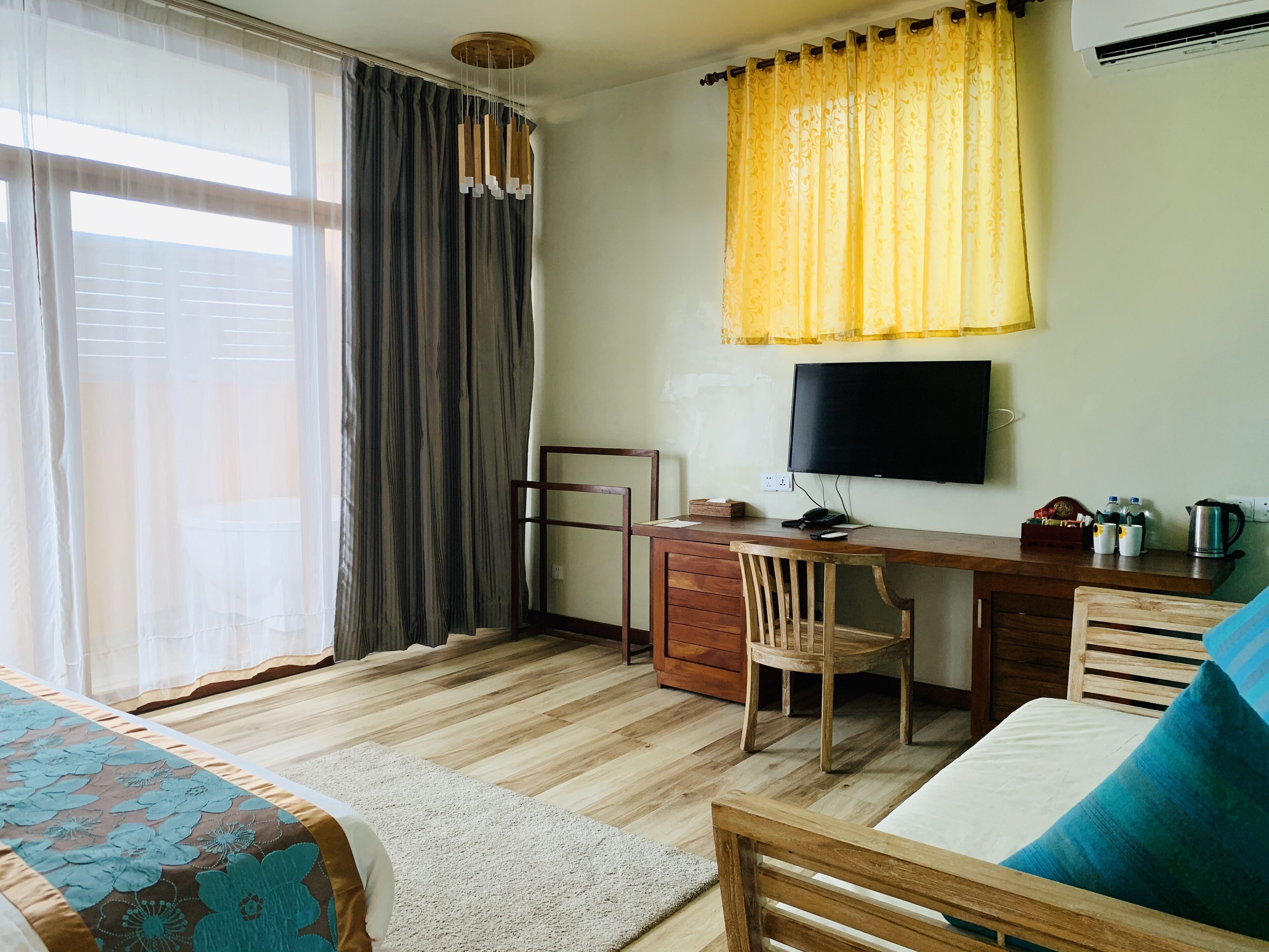 Une chambre avec un lit, un bureau et une chaise, une télévision et une fenêtre avec des rideaux.