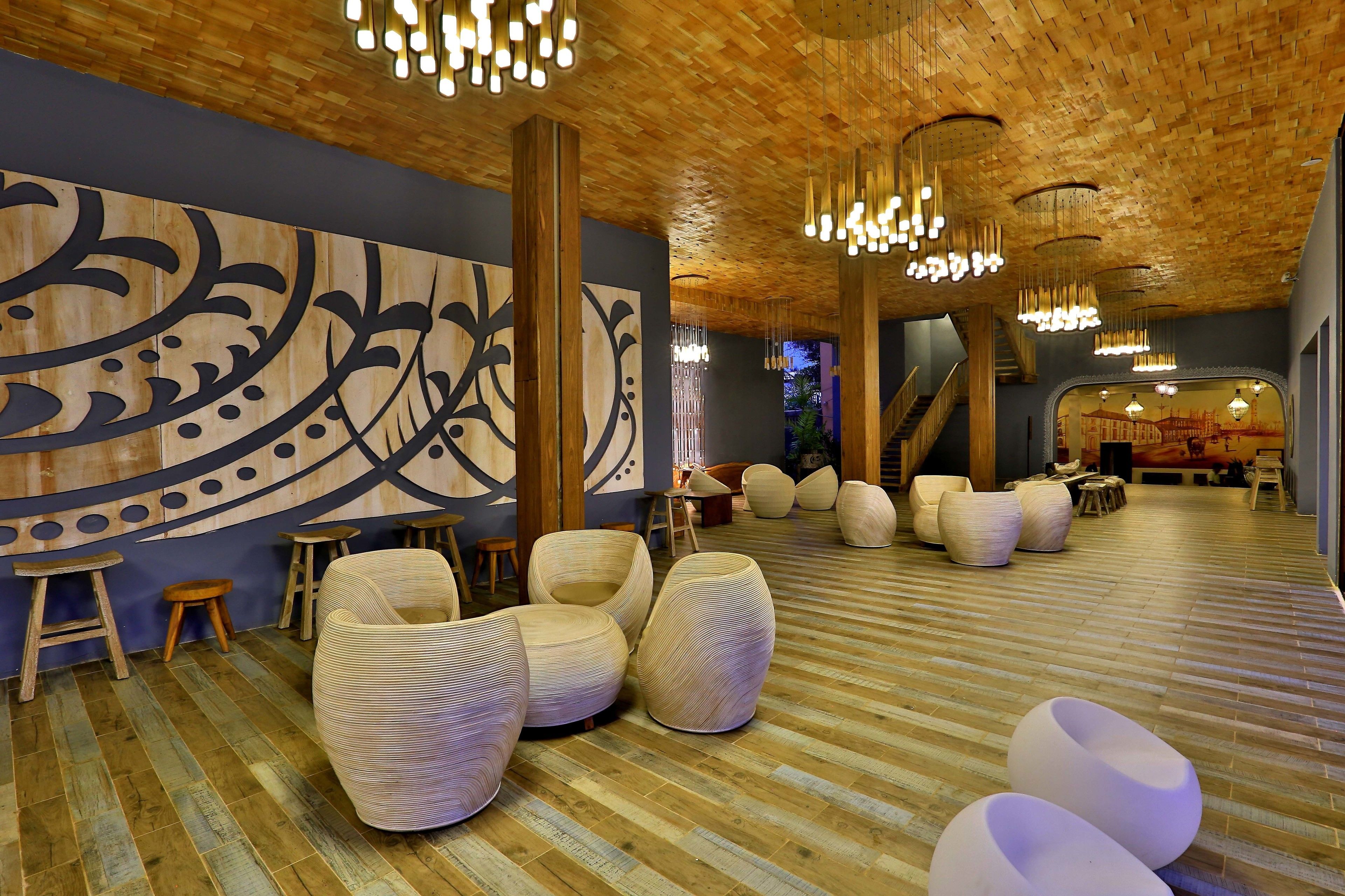 A spacious lobby with a wooden floor, large woven chairs, and a prominent abstract wall art piece.