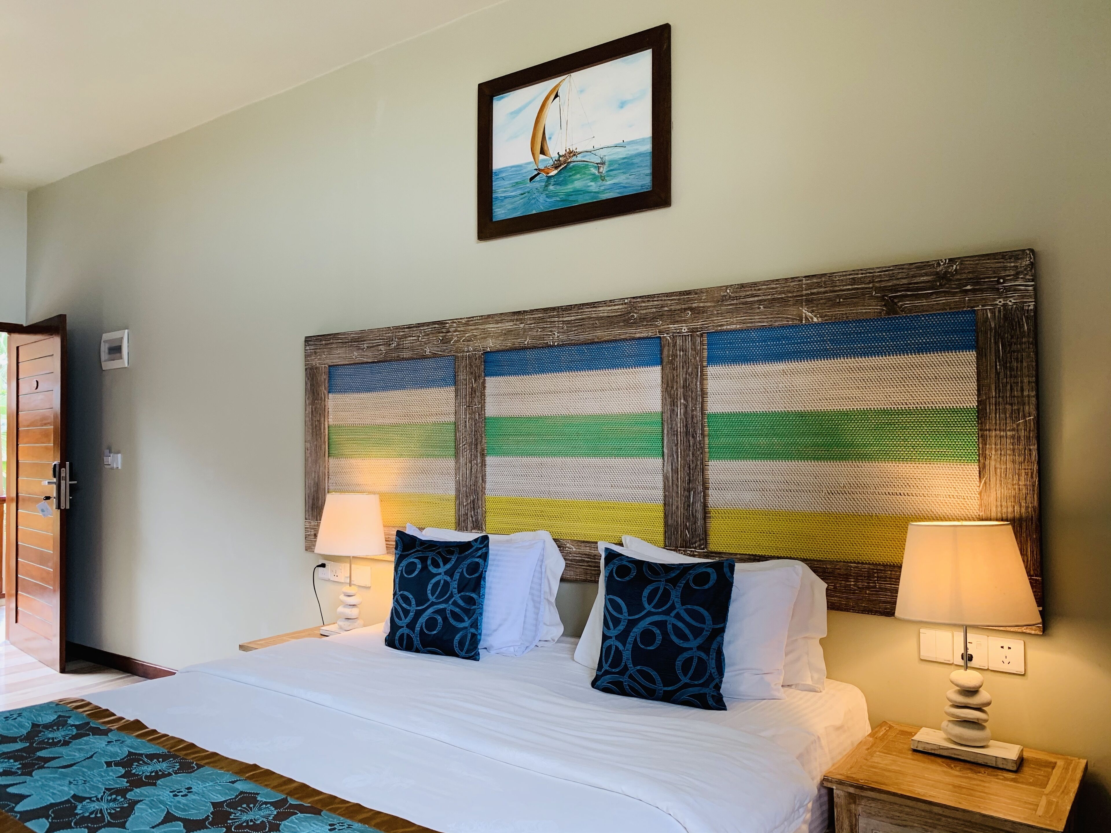 A hotel room with a bed, two bedside lamps, a wall-mounted painting, and a wooden headboard.