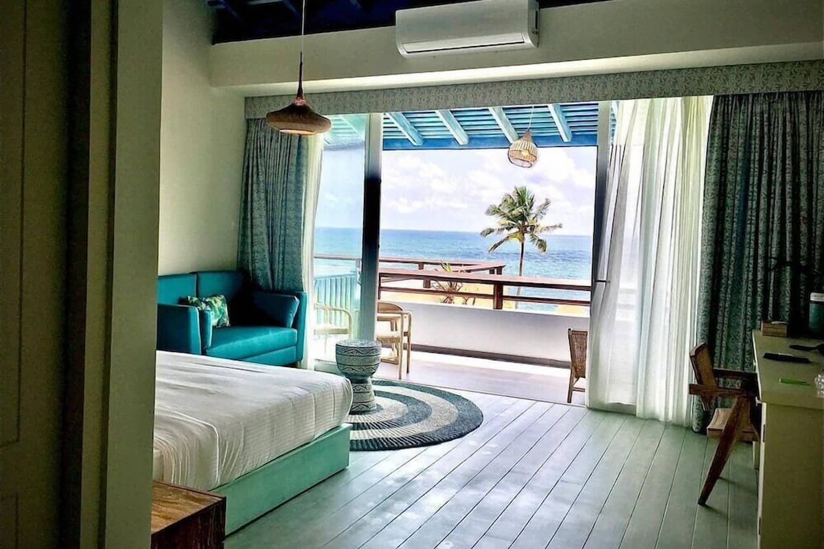 A room with a bed, a sofa, a dining table, and a view of the ocean.