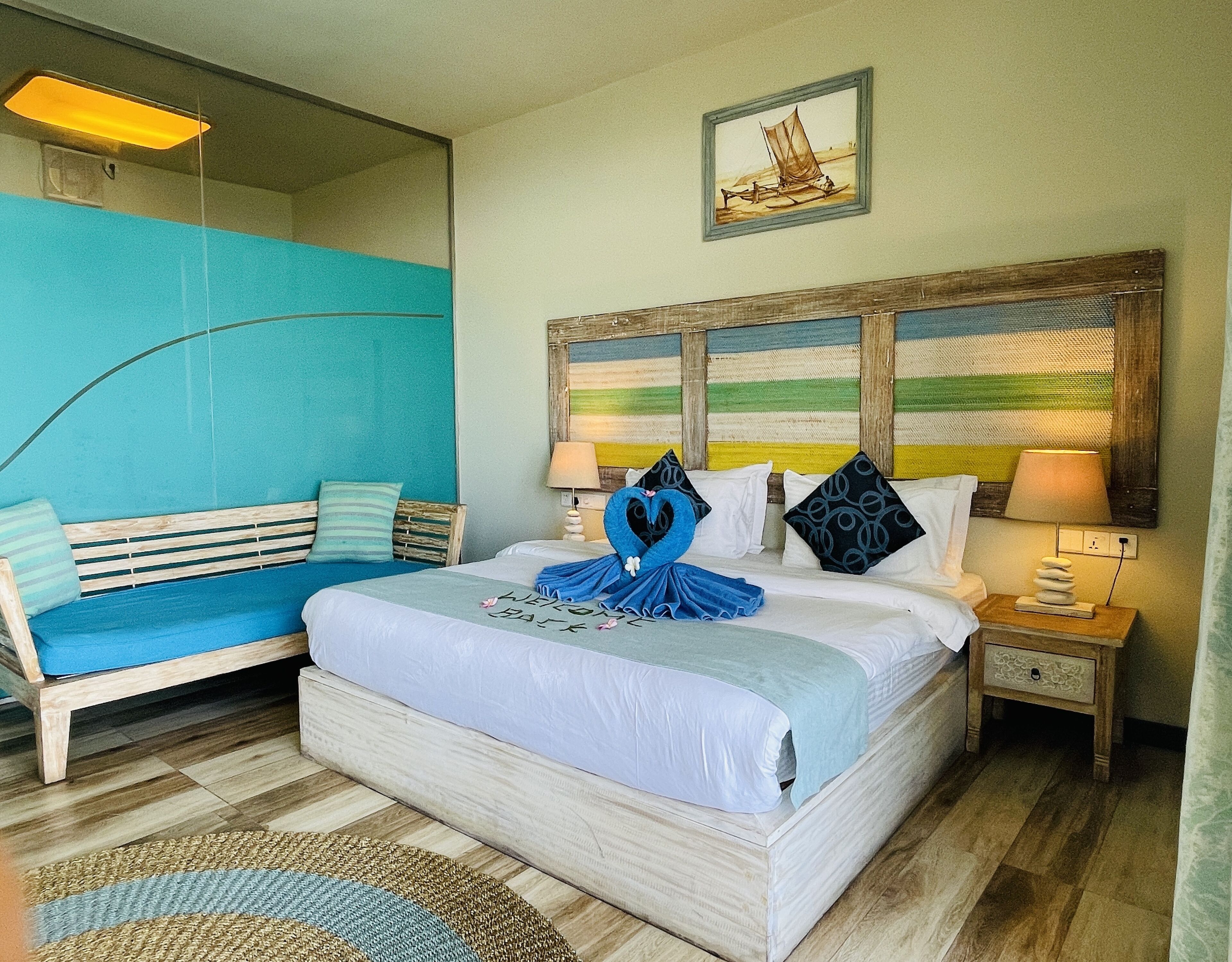 A hotel room with a bed, a bench, a lamp, and a painting on the wall.