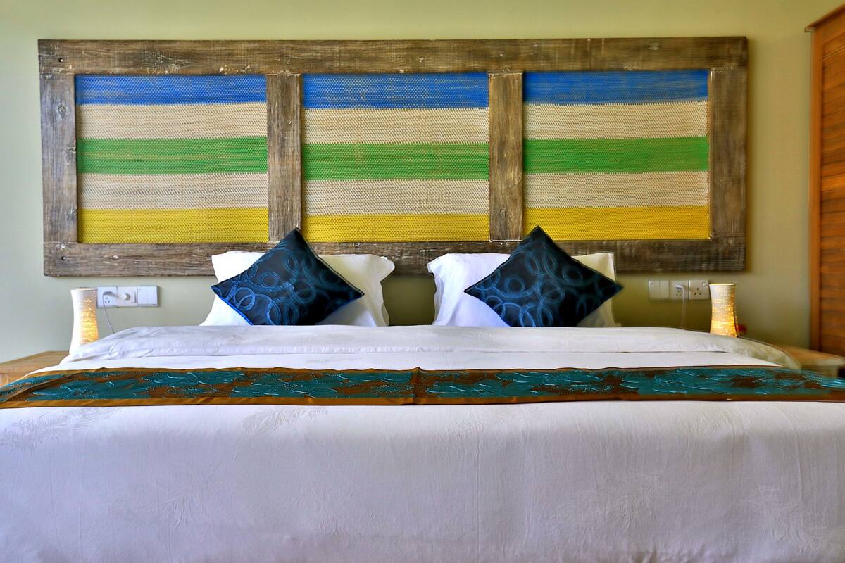 A bed with white bedding, two blue patterned pillows, and a decorative headboard with a striped design.
