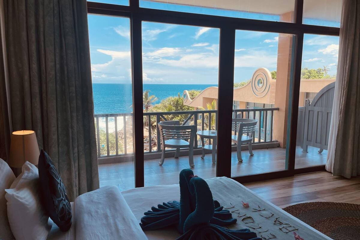 A hotel room with a large window overlooking a balcony with outdoor furniture.