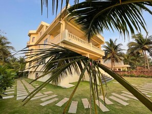 A multi-story building with a balcony, surrounded by a well-maintained lawn and palm trees. - Kay's By The Sea (Vengurla)