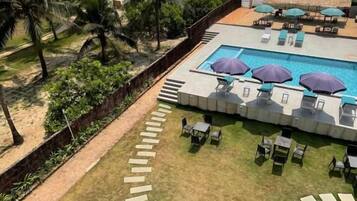 Un espace piscine avec des chaises longues et des parasols, un chemin menant à la piscine et une vue sur l’océan.