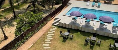 A pool area with lounge chairs and umbrellas, a pathway leading to the pool, and a view of the ocean.