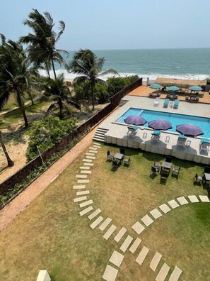 A pool area with lounge chairs and umbrellas, a pathway leading to the pool, and a view of the ocean. - Kay's By The Sea (Vengurla)