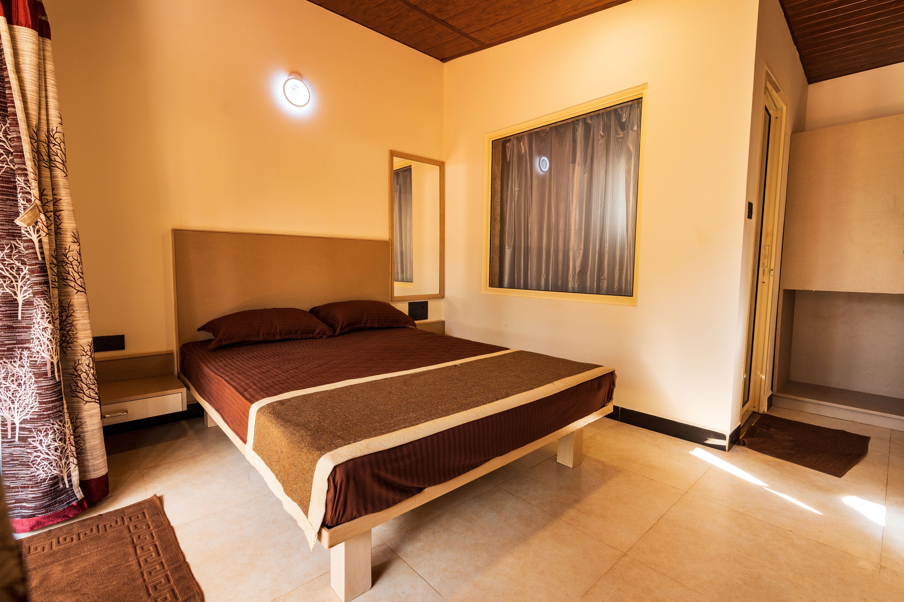 Une chambre à coucher comprenant un lit, une table de chevet, une commode, une fenêtre avec des rideaux et une porte.