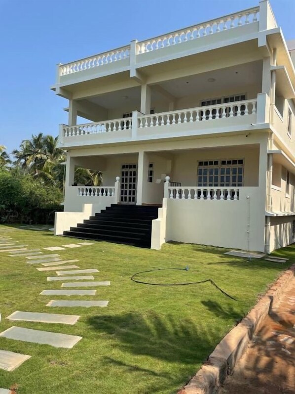 A two-story building with a balcony, a staircase leading to the entrance, and a well-maintained lawn. - Kay's By The Sea (Vengurla)
