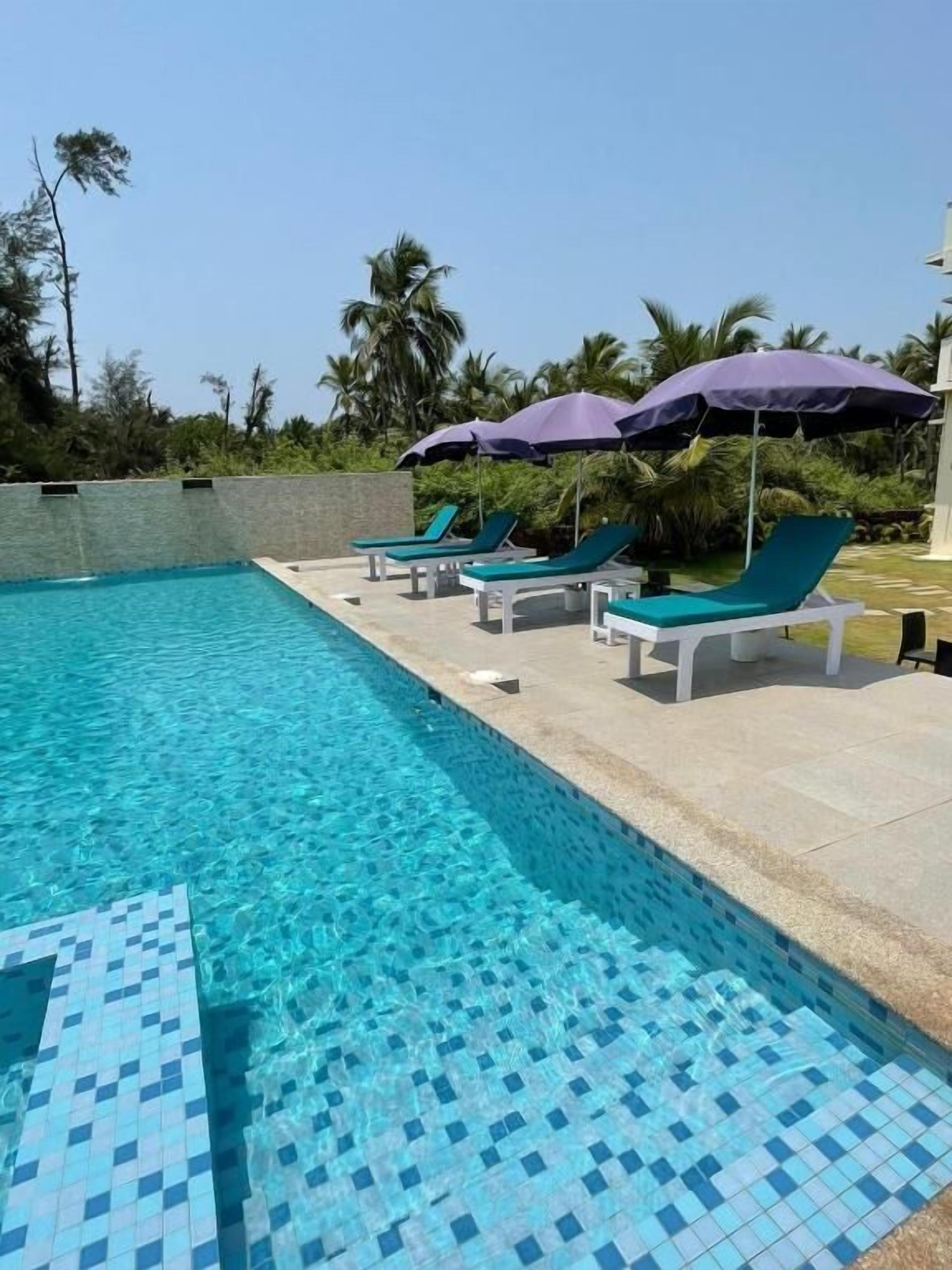 A swimming pool with clear blue water, surrounded by lounge chairs and umbrellas.