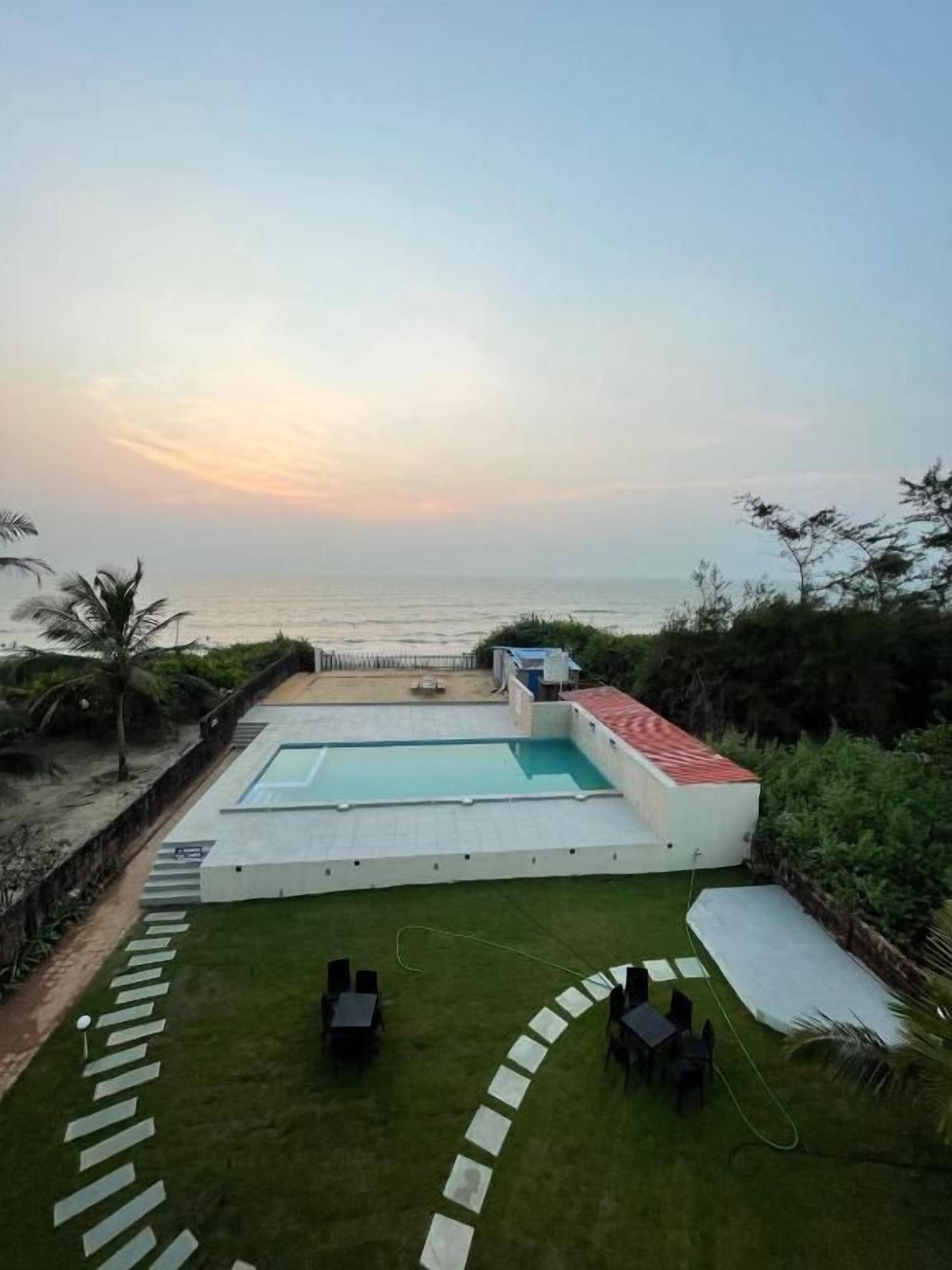 Una piscina con vistas al mar, rodeada de un césped cuidado y algunas sillas.