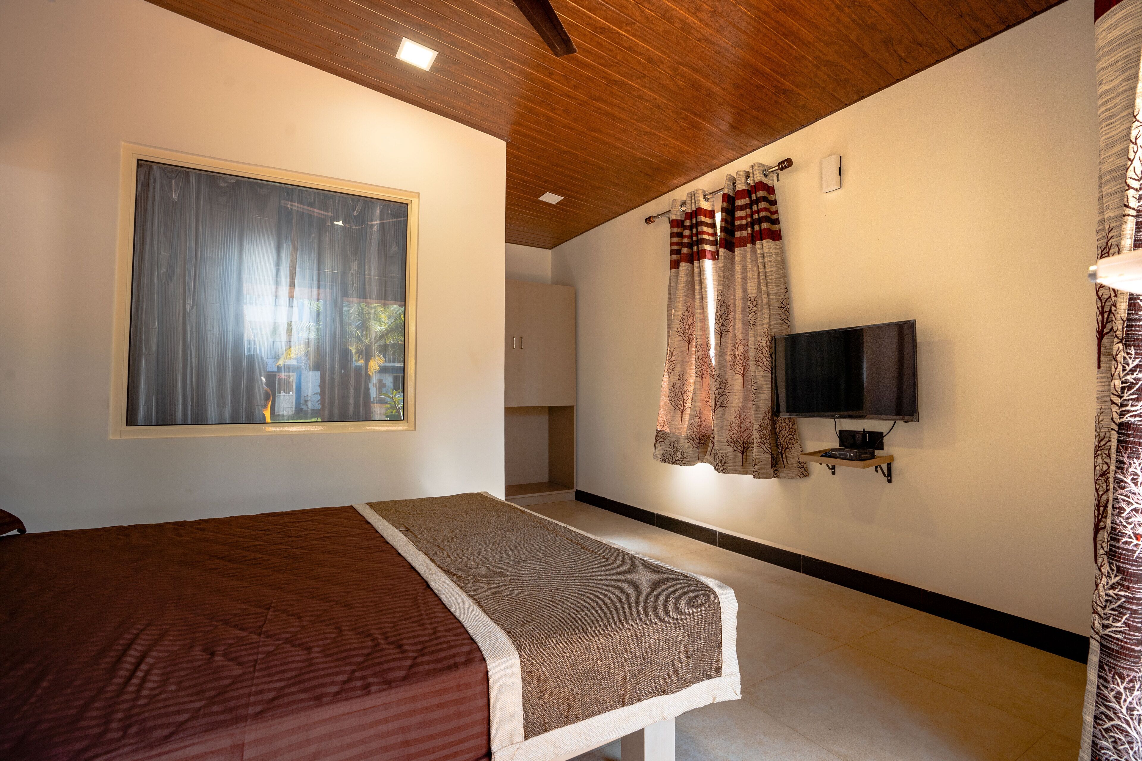 A bedroom with a bed, a TV mounted on the wall, and a window with curtains.