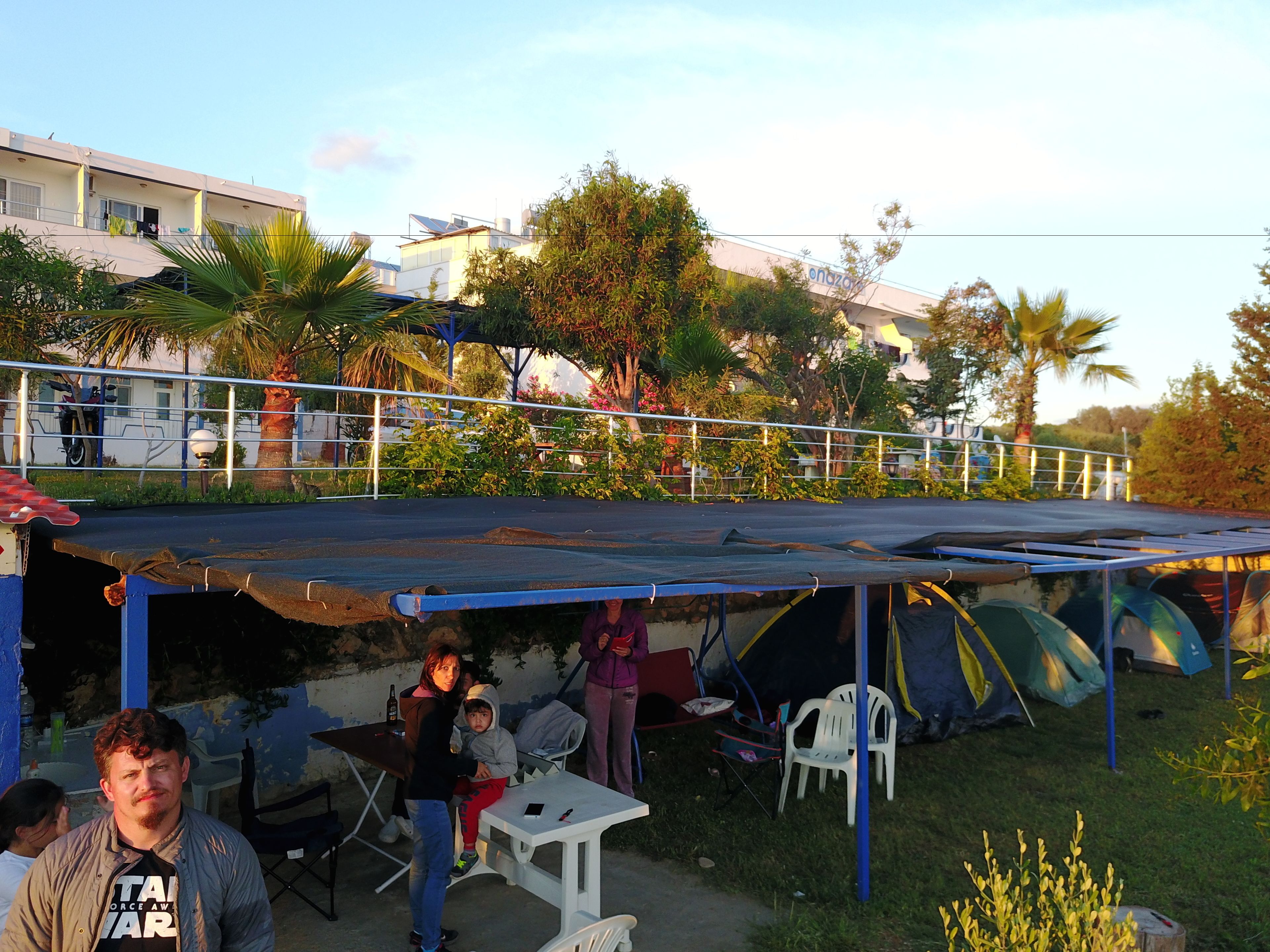 Zona coberta a l'exterior amb una taula, cadires, una tenda petita i un edifici al fons.