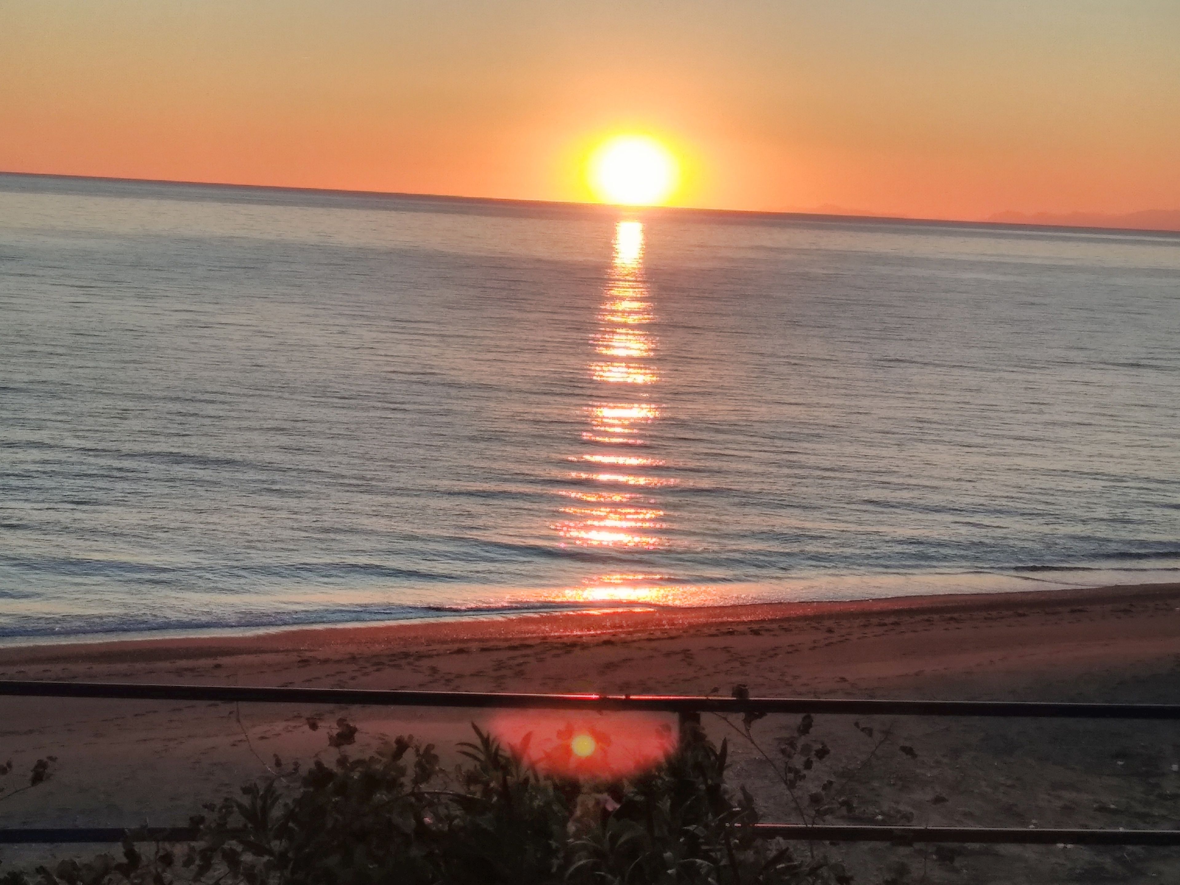 A sunset over a calm sea with a beach in the foreground.