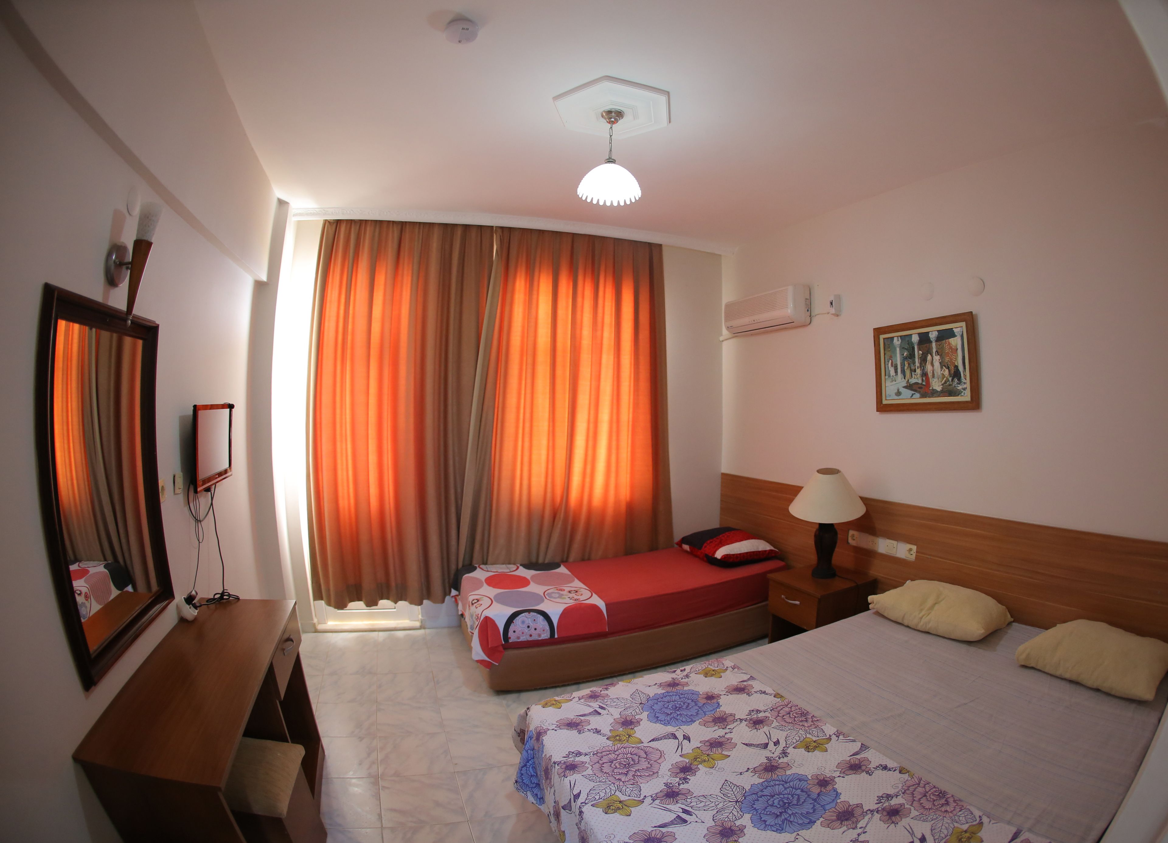 A hotel room with two beds, a wooden headboard, a nightstand, a lamp, a mirror, and a painting on the wall.