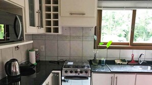 Une cuisine équipée d’une cuisinière, d’un four et d’un évier. Une fenêtre offre une vue sur les arbres.